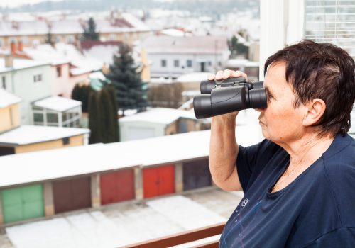 Senior woman with binoculars looking out window